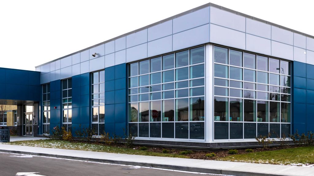 A school building with blue and grey metal cladding. There are large windows throughout the structure.