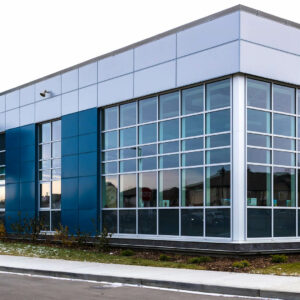 A school building with blue and grey metal cladding. There are large windows throughout the structure.