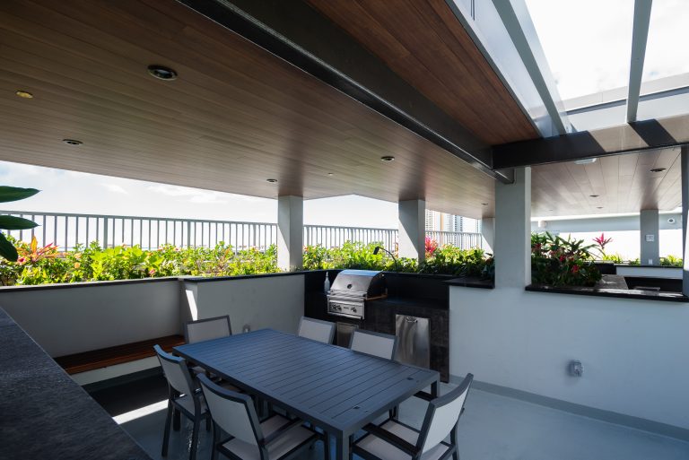 External area of a building with barbecue grill, a table with 6 chairs and aluminum metal plank in the soffit